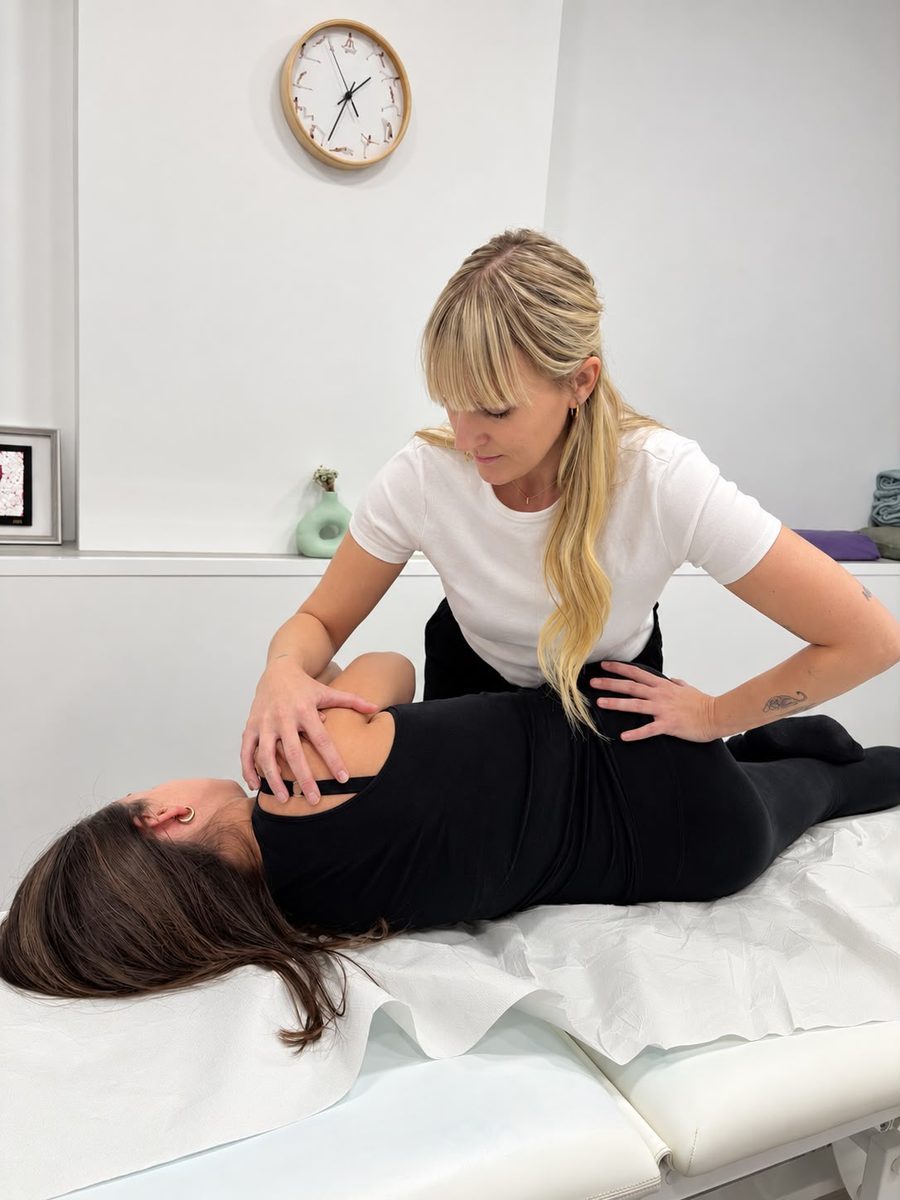Isabel aplicando terapia manual en el hombro y la espalda de una paciente tumbada de lado en la camilla